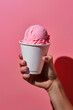 Woman's hand holding pink ice cream in cup in front of studio background