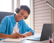© Monkey Business - Teenage Boy Sitting At Desk In Bedroom At Home Doing Homework Streaming Music To Headphones