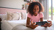 © Monkey Business - Teenage Girl Lying On Bed At Home Playing With Handheld Gaming Device