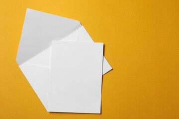 Wall Mural - Blank sheet of paper and letter envelope on orange background, top view. Space for text