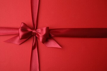 Wall Mural - Bright satin ribbon with bow on red background, top view