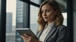© Tehmas - Attractive young businesswoman using a digital tablet while standing in front of windows in office