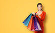 © vgstudio - Portrait image beautiful young woman wearing orange dress clothes standing isolated against over yellow background, carrying rising showing colorful shopping bags. Sales, rebates offers ad concept.