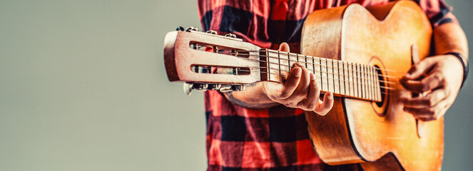 Guitarist, music.Young man plays an acoustic guitar on a gray isolated background. Man's hands playing acoustic guitar, close up. Acoustic guitars playing