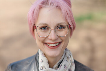 close-up portrait of young beautiful caucasian woman with coloured pink hair in park smiling widely