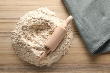 Pile of flour and rolling pin on wooden table, top view