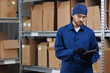 Worker in blue uniform use clipboard for control box in warehouse storage. Concept logistic center and delivery