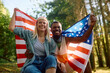 Cheerful multiracial couple with US flag in nature looking at camera.