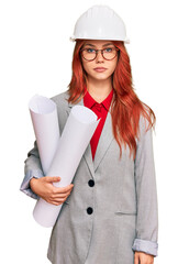 Poster - Young redhead architect woman wearing safety helmet holding blueprints thinking attitude and sober expression looking self confident