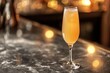 Photo of a champagne flute filled with a yellow cocktail, sitting on the edge of a bar counter with bokeh background and copy space.