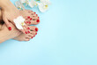 Woman with stylish red toenails after pedicure procedure and orchid flowers on light blue background, top view. Space for text
