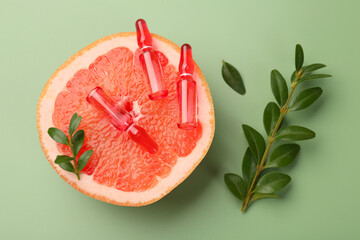 Skincare ampoules with vitamin C, half of grapefruit and leaves on light green background, flat lay