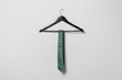 Hanger with green necktie on light grey wall