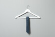Hanger with blue necktie on light grey wall