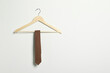 Hanger with striped necktie on white wall. Space for text
