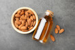 Almond oil in bottle and bowl with nuts on grey textured table, flat lay
