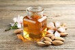Almond oil in bottle, flowers and nuts on wooden table, closeup