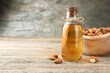 Almond oil in bottle and nuts on wooden table, closeup. Space for text