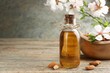 Almond oil in bottle, flowers and nuts on wooden table, closeup. Space for text
