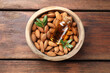 Bowl with almond oil in bottle, leaves and nuts on wooden table, top view