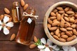 Almond oil in bottles, flowers and bowl with nuts on wooden table, flat lay