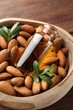 Bowl with almond oil in bottle, leaves and nuts on wooden table, closeup