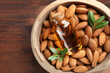 Bowl with almond oil in bottle, leaves and nuts on wooden table, top view. Space for text