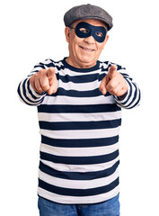 Wall Mural - Senior handsome man wearing burglar mask and t-shirt pointing to you and the camera with fingers, smiling positive and cheerful