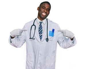 Wall Mural - Young african american man wearing doctor uniform and stethoscope looking confident with smile on face, pointing oneself with fingers proud and happy.