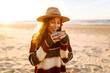 © maxbelchenko - Young woman sits at picnic on the beach drinks a hot drink from a thermos. A girl enjoying beautiful view of the sea. Travel, weekend, relax and lifestyle concept