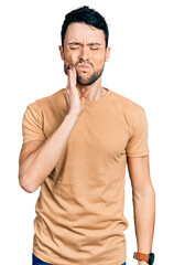 Poster - Hispanic man with beard wearing casual t shirt touching mouth with hand with painful expression because of toothache or dental illness on teeth. dentist