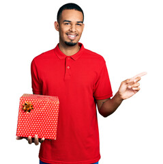 Wall Mural - Young african american man holding gift smiling happy pointing with hand and finger to the side