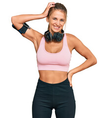 Wall Mural - Young blonde woman wearing gym clothes and using headphones confuse and wonder about question. uncertain with doubt, thinking with hand on head. pensive concept.