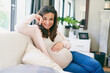 Happy, woman and pregnancy with hand on stomach for connection, love and care for baby on sofa at home. Health, female person or new mother with belly for relax, growth and comfort in living room