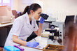 Microscope, female scientist and analyse in laboratory for research or medical breakthrough. Notes, data and health with doctor or expert in microbiology with equipment for clinical trial in America.