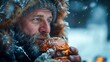 A man with a beard is eating a hamburger in the snow