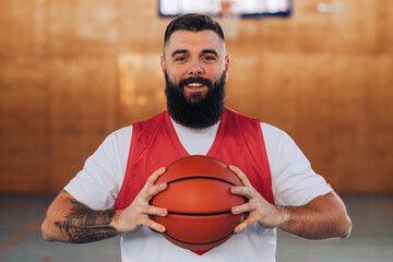 Wall Mural - Portrait of a smiling caucasian bearded basketball player holding a ball