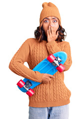 Wall Mural - Young beautiful mixed race woman holding skate covering mouth with hand, shocked and afraid for mistake. surprised expression