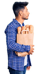 Canvas Print - Handsome latin american young man holding paper bag with bread looking to side, relax profile pose with natural face and confident smile.