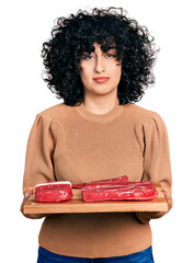 Canvas Print - Young middle east girl holding board with raw meat relaxed with serious expression on face. simple and natural looking at the camera.