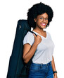 © Krakenimages.com - Young african american woman wearing guitar case looking positive and happy standing and smiling with a confident smile showing teeth