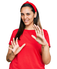 Wall Mural - Young hispanic woman wearing casual clothes disgusted expression, displeased and fearful doing disgust face because aversion reaction. with hands raised