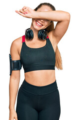 Beautiful blonde woman wearing gym clothes and using headphones covering eyes with arm smiling cheerful and funny. blind concept.