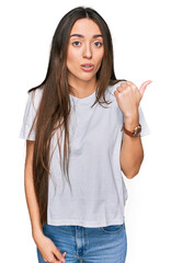 Canvas Print - Young hispanic girl wearing casual white t shirt surprised pointing with hand finger to the side, open mouth amazed expression.