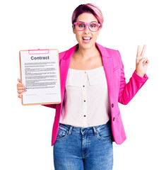 Wall Mural - Young beautiful woman with pink hair holding clipboard with contract document smiling looking to the camera showing fingers doing victory sign. number two.