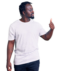 Canvas Print - Young african american man with braids wearing casual white tshirt looking proud, smiling doing thumbs up gesture to the side