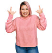 © Krakenimages.com - Hispanic woman with pink hair wearing casual winter sweater shouting with crazy expression doing rock symbol with hands up. music star. heavy music concept.