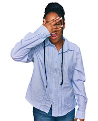 Canvas Print - Young african american woman wearing casual clothes peeking in shock covering face and eyes with hand, looking through fingers with embarrassed expression.