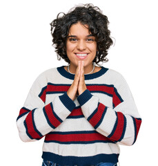 Canvas Print - Young hispanic woman with curly hair wearing casual clothes praying with hands together asking for forgiveness smiling confident.