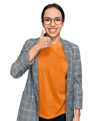 Wall Mural - Young hispanic girl wearing business jacket and glasses doing happy thumbs up gesture with hand. approving expression looking at the camera showing success.